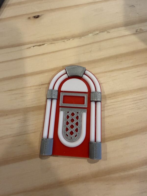 Small red, white and grey 3D printed jukebox at dollhouse scale on a wooden surface.