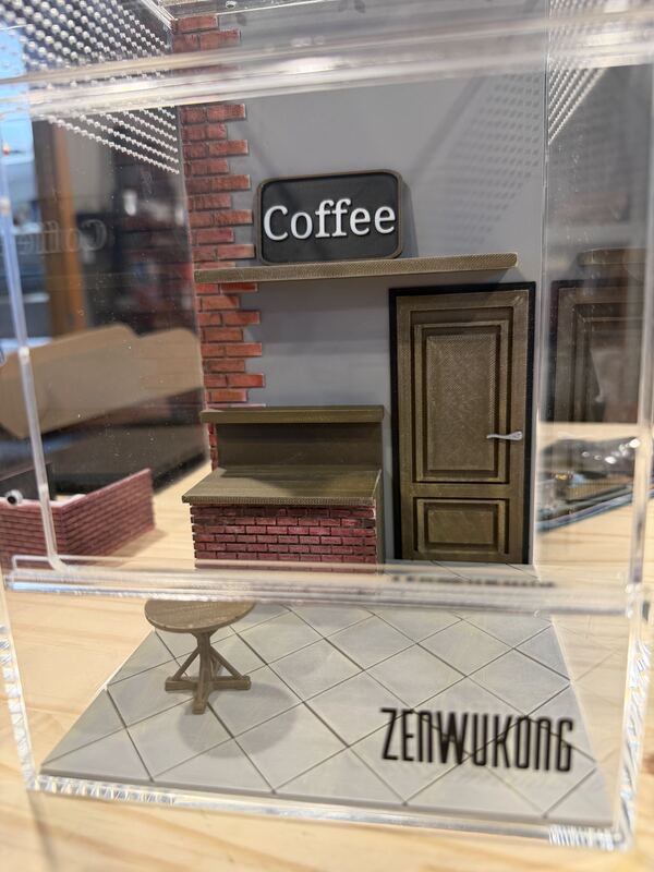 Miniature 3D printed coffee shop facade with brick wall, wooden door, hanging Coffee sign and tiled floor.